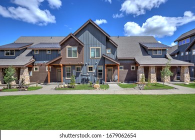 Newly Build Modern And Rustic Home From Exterior In Natural Brown And Grey Colors With Walkways, Green Grass And Natural Stone.  Blue Sky And Sunny Day. American New Archtecture.