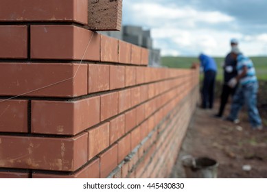 Newly Built Red Brick Wall Of A Newly Built House With Bricklayers In The Background