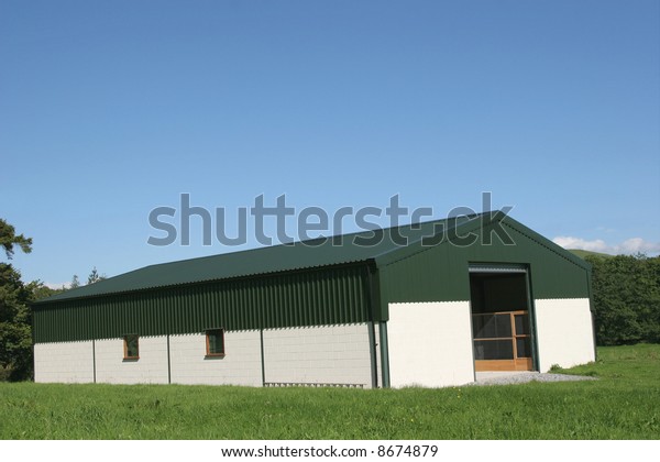 Newly constructed barn of cream painted concrete
block walls with a green metal sheet roof,set against a blue sky
and trees to the rear.
