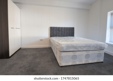 A newly decorated typical British UK bedroom with a large bed and wardrobe, with white walls with blinds at the window.
