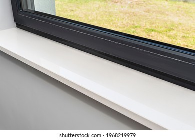Newly installed white conglomerate window sill inside the room, on the gray walll, visible grass outside the window. - Shutterstock ID 1968219979