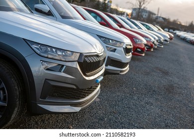 Newly made passenger SUVs cars parked in a row among other manufacturer models awaiting it's final pre-sale preparation. Visible transportation logistic protective equipment. Dusk light. Car front.