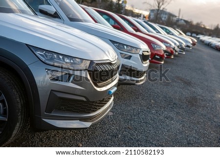 Newly made passenger SUVs cars parked in a row among other manufacturer models awaiting it's final pre-sale preparation. Visible transportation logistic protective equipment. Dusk light. Car front.