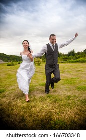 Newly married couple running and jumping in park while holding hands