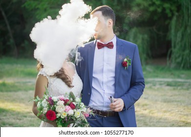 Newly wedded couple, the groom is smoking vape, their heads in the cigar fumes, smoking wedding concept, vaping concept