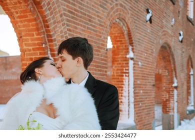 Newlywed couple embraces kisses under beautiful brick arches in snowy landscape their elegant attire contrasts with rustic surroundings, creating magical atmosphere. - Powered by Shutterstock