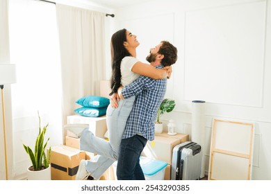 Newlywed couple embraces and laughs in their new home, surrounded by moving boxes, eagerly anticipating the start of their life together - Powered by Shutterstock