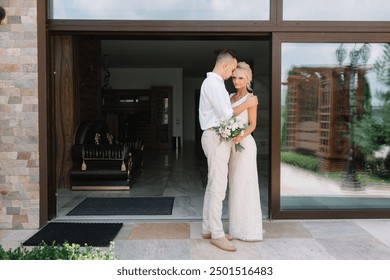 Newlywed couple embracing on their wedding day outside their home, radiating love and happiness. The bride holds a bouquet, creating a romantic and joyful scene. - Powered by Shutterstock