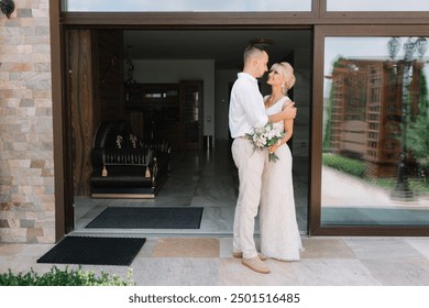 Newlywed couple embracing on their wedding day outside their home, radiating love and happiness. The bride holds a bouquet, creating a romantic and joyful scene. - Powered by Shutterstock