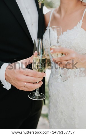 Newlyweds clinking glasses and enjoying romantic moment together at wedding reception outside. Bride and groom drinking champagne at wedding party.