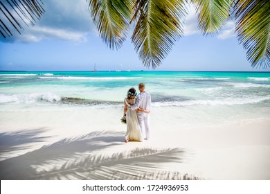Newlyweds holding hands hugging at white sandy tropical caribbean beach landscape after wedding ceremony of marriage on destination wedding honeymoon travel looking on blue sea in Punta Cana Dominican