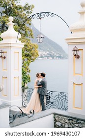 Newlyweds hug and almost kiss under an old arch against the backdrop of Lake Como. Side view