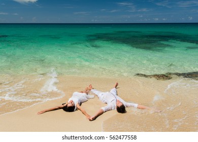 Newlyweds lie on the sand near coastal rocks of caribbean azure sea at summer sunny day - Shutterstock ID 562477558