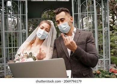 Newlyweds In Protective Masks Showing Wedding Rings During Video Chat On Laptop