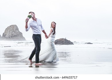 The newlyweds are running by the ocean while the groom is smelling flowers and holding his bride by her hand