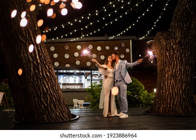 newlyweds with sparklers in a night park with garlands on the trees. A perfect end to the wedding day. shooting in the dark. the bride in a white elegant dress and the groom in a blue suit. - Powered by Shutterstock