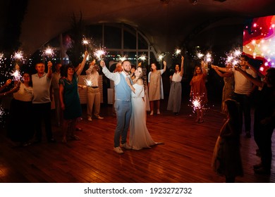 newlyweds with sparklers say goodbye to guests in the night restaurant. beautiful end to the wedding day. Groom in a blue suit and bride in white elegant dress. shooting in the dark. 
