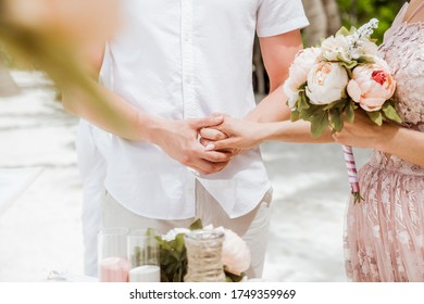 Newlyweds At The Wedding Romantic Couple Holding Hands During Destination Wedding Marriage Matrimonial Ceremony On The Sandy Beach In Dominican Republic, Punta Cana. Family, Love, Unity Concept.  