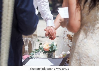 Newlyweds At The Wedding Romantic Couple Holding Hands During Destination Wedding Marriage Matrimonial Ceremony On The Sandy Beach In Dominican Republic, Punta Cana. Family, Love, Unity Concept.  