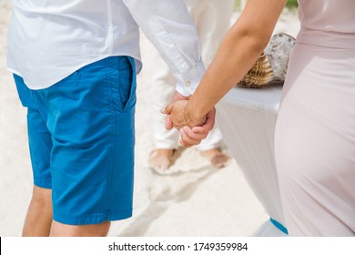 Newlyweds At The Wedding Romantic Couple Holding Hands During Destination Wedding Marriage Matrimonial Ceremony On The Sandy Beach In Dominican Republic, Punta Cana. Family, Love, Unity Concept.  