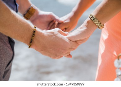 Newlyweds At The Wedding Romantic Couple Holding Hands During Destination Wedding Marriage Matrimonial Ceremony On The Sandy Beach In Dominican Republic, Punta Cana. Family, Love, Unity Concept.  