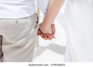 Newlyweds At The Wedding Romantic Couple Holding Hands During Destination Wedding Marriage Matrimonial Ceremony On The Sandy Beach In Dominican Republic, Punta Cana. Family, Love, Unity Concept.  