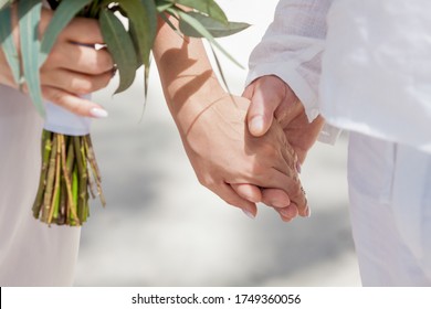 Newlyweds At The Wedding Romantic Couple Holding Hands During Destination Wedding Marriage Matrimonial Ceremony On The Sandy Beach In Dominican Republic, Punta Cana. Family, Love, Unity Concept.  