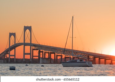 Newport Bridge at sunset in Newport, Rhode Island, a popular tourist destination in New England. A sailboat is at the mooring in front of the bridge. Nautical and coastal scene with boats and bridge. 