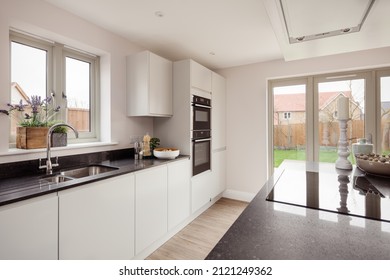 Newport, Essex - March 21 2019: Luxury Modern Kitchen Within Brand New Staged Home With Peninsular Unit, Integrated Built In Appliances And Doors Leading To Patio And Garden.