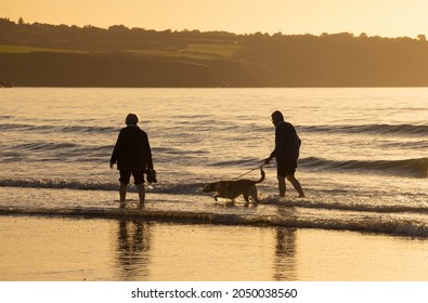Newport, Pembrokeshire, Wales, UK. September 23rd 2021. Middle aged couple walking their dog on the shore at Newport Sands Beach in the early evening. 