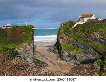 Newquay, Cornwall. Ciffs with bridge spanning between houses. Sea, sky, sandy beach, February. UK