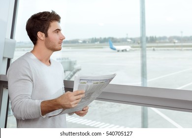 News On The Go. Horizontal Portrait Of A Handsome Young Guy With A Newspaper Waiting For His Flight At The Airport Departure Lounge Standing Near The Window Copyspace