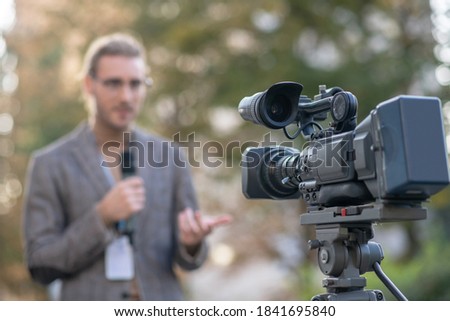 News reporter. Fair-haired male reporter speaking into microphone in front of camera outside