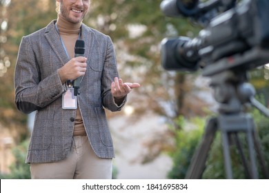 News Reporter. Male Reporter Speaking Into Microphone In Front Of Camera Outside