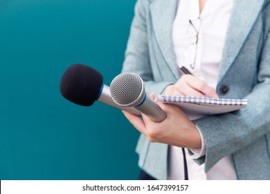 News reporter or TV journalist at press conference, holding microphone and writing notes