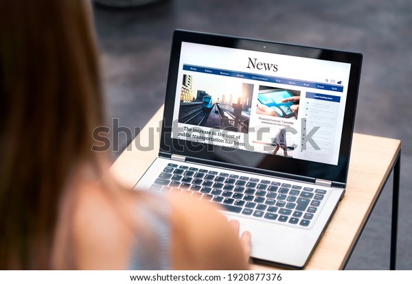 News website in laptop screen with online article\
and headline. Woman reading newspaper or magazine with computer.\
Digital web publication portal and internet page. Latest daily\
media site mockup.