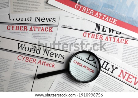 Newspaper with headline CYBER ATTACK and magnifying glass, top view