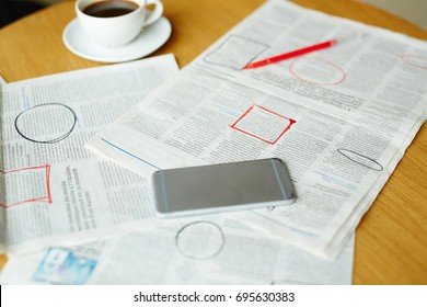 Newspaper with highlighted vacancy adverts, smartphone, cup of coffee and pen on table