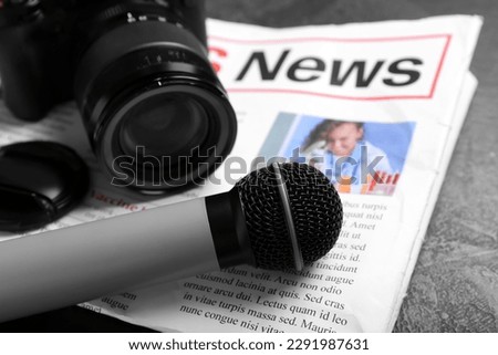Newspaper with microphone and photo camera on dark background, closeup