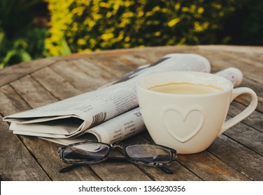 Newspaper, reading glasses and a cup of coffee on a wooden table, outdoors. - Powered by Shutterstock