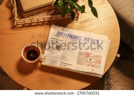 Newspaper with tea cup on table in dark living room, top view