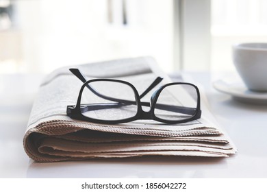 Newspapers and coffee cup, with reading glasses.	