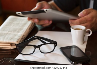 Newspapers and coffee cup, reading glasses, striped paper, hands holding tablet, cell phone. - Powered by Shutterstock