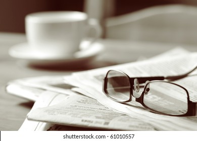 Newspapers and coffee cup, with reading glasses.  Toned image, focus on reading glasses.