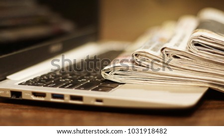 Newspapers and computer. Laptop and daily papers on the table. Fresh news by  paper or by electronic device, different ways of communication. Source of information, actual data on pages or on screen 