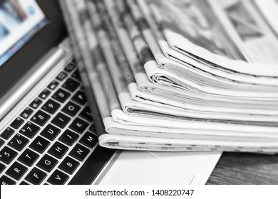 Newspapers and laptop. Pile of daily papers with news on the computer. Pages with headlines, articles folded and stacked on keypad of electronic device. Modern gadget and old journals, focus on paper 