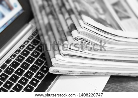 Newspapers and laptop. Pile of daily papers with news on the computer. Pages with headlines, articles folded and stacked on keypad of electronic device. Modern gadget and old journals, focus on paper 
