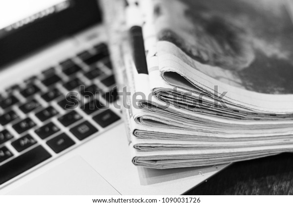 Newspapers and laptop. Pile of daily papers with\
news on the computer. Pages with headlines, articles folded and\
stacked on keypad of electronic device. Modern gadget and old\
journals, focus on\
paper