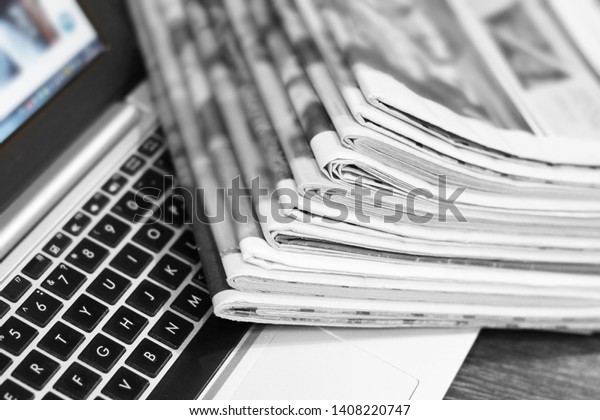 Newspapers and laptop. Pile of daily papers with news on\
the computer. Pages with headlines, articles folded and stacked on\
keypad of electronic device. Modern gadget and old journals, focus\
on paper 