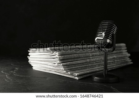 Newspapers and vintage microphone on dark stone table. Journalist's work